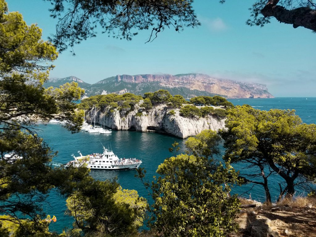 Breathtaking view of Cassis coast featuring a white yacht and lush greenery under a clear blue sky.